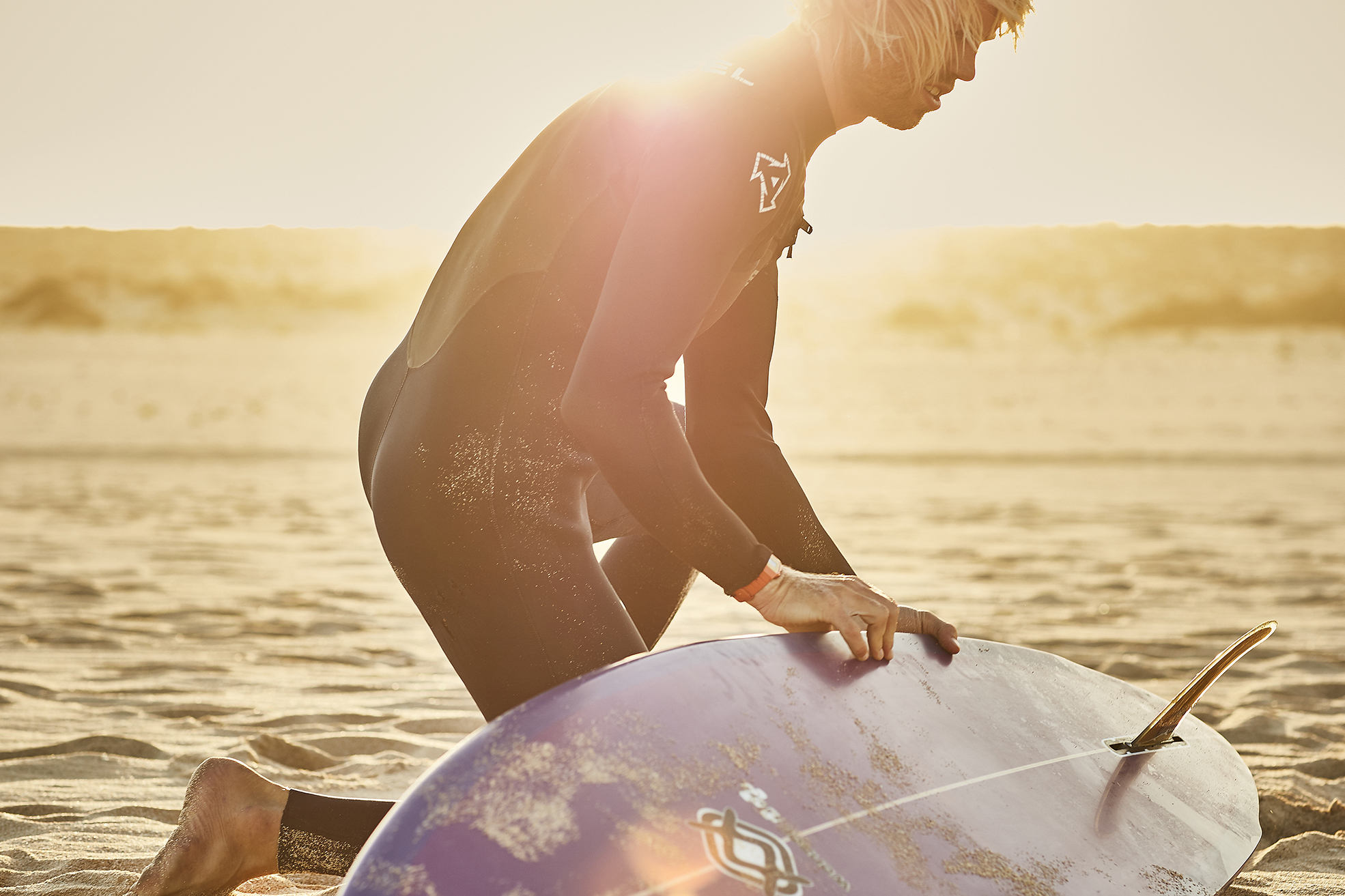surfer waxing his board at sunset